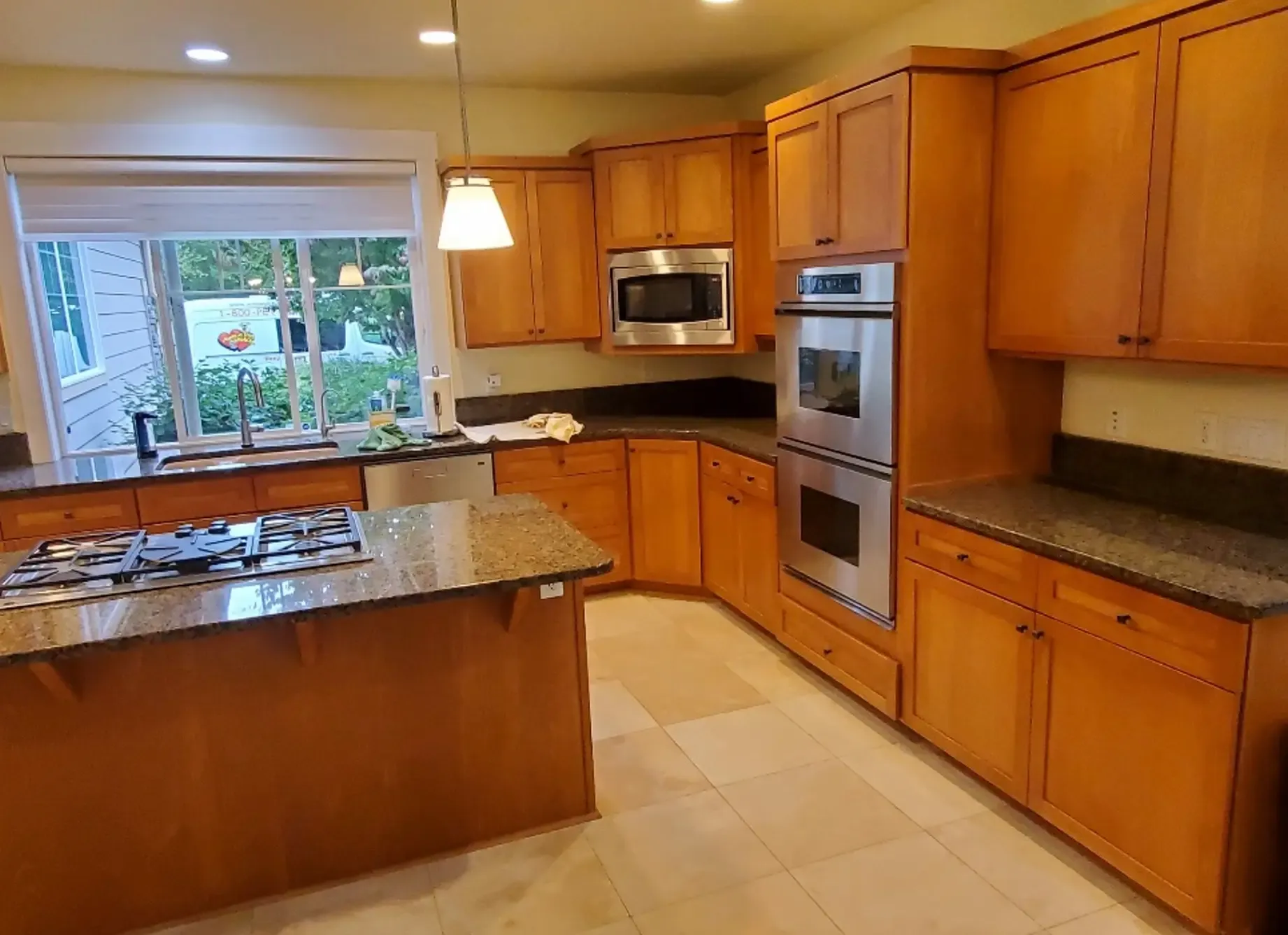 a dated-looking kitchen with stained wooden cabinets, a dark granite countertop, and hanging lamps